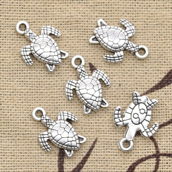 A collection of silver vintage sea turtle charms for jewelry making displayed on a burlap background.