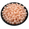 A pile of translucent pink acrylic round beads for jewelry making in a black bowl.