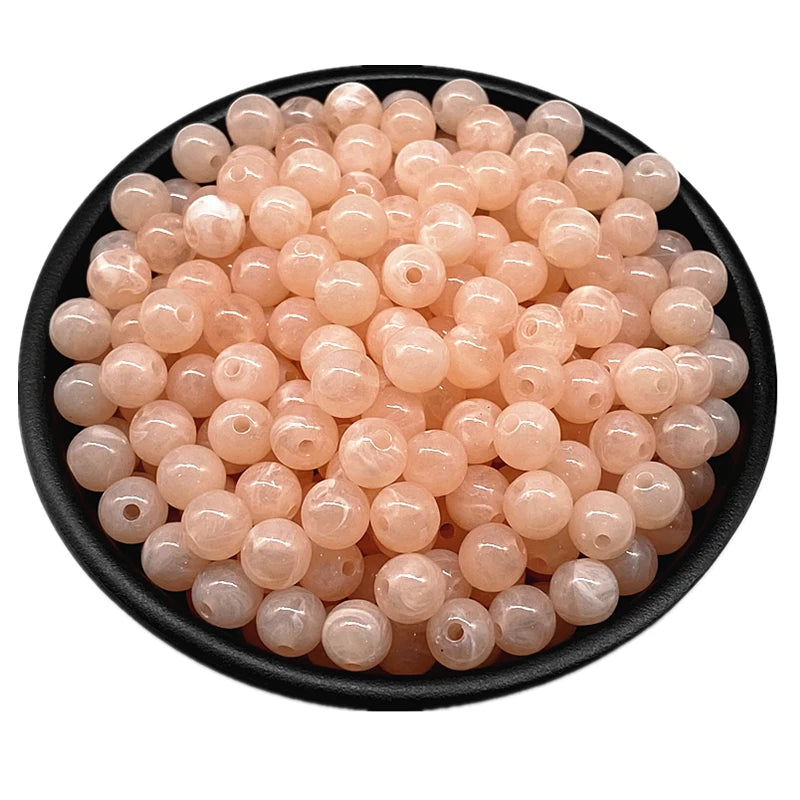 A pile of translucent pink acrylic round beads for jewelry making in a black bowl.