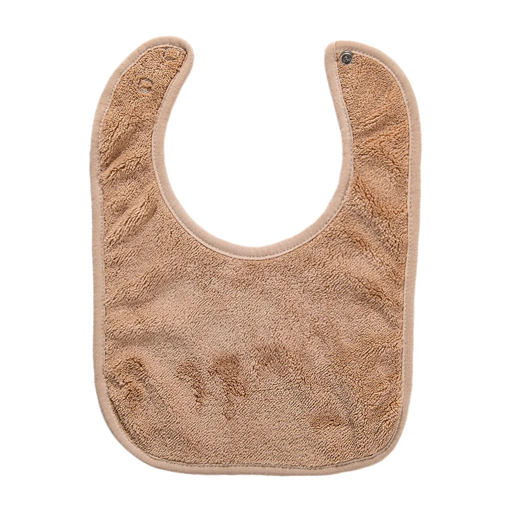 A beige soft cotton baby bib with a rounded shape and adjustable snap closure.
