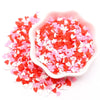 A pink bowl filled with red and white heart-shaped polymer clay sprinkles for craft decorating.
