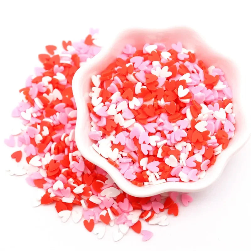 A pink bowl filled with red and white heart-shaped polymer clay sprinkles for craft decorating.
