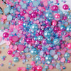 A pile of mixed resin rhinestone pearls in various shades of pink, blue, and purple with an AB finish for crafts and nail art