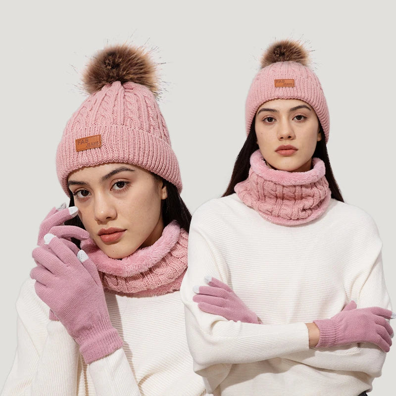 A woman models a pink knit winter hat, scarf, and gloves set with a faux fur pom on a light background.