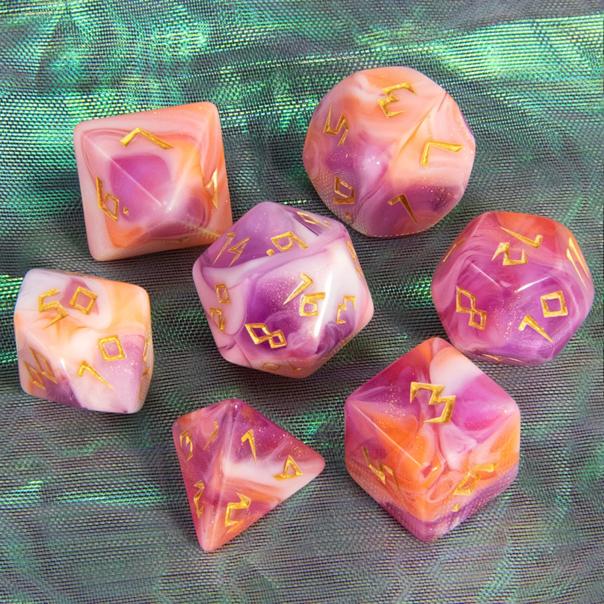 A set of seven translucent pink and purple glitter polyhedral dice resting on a green fabric surface.