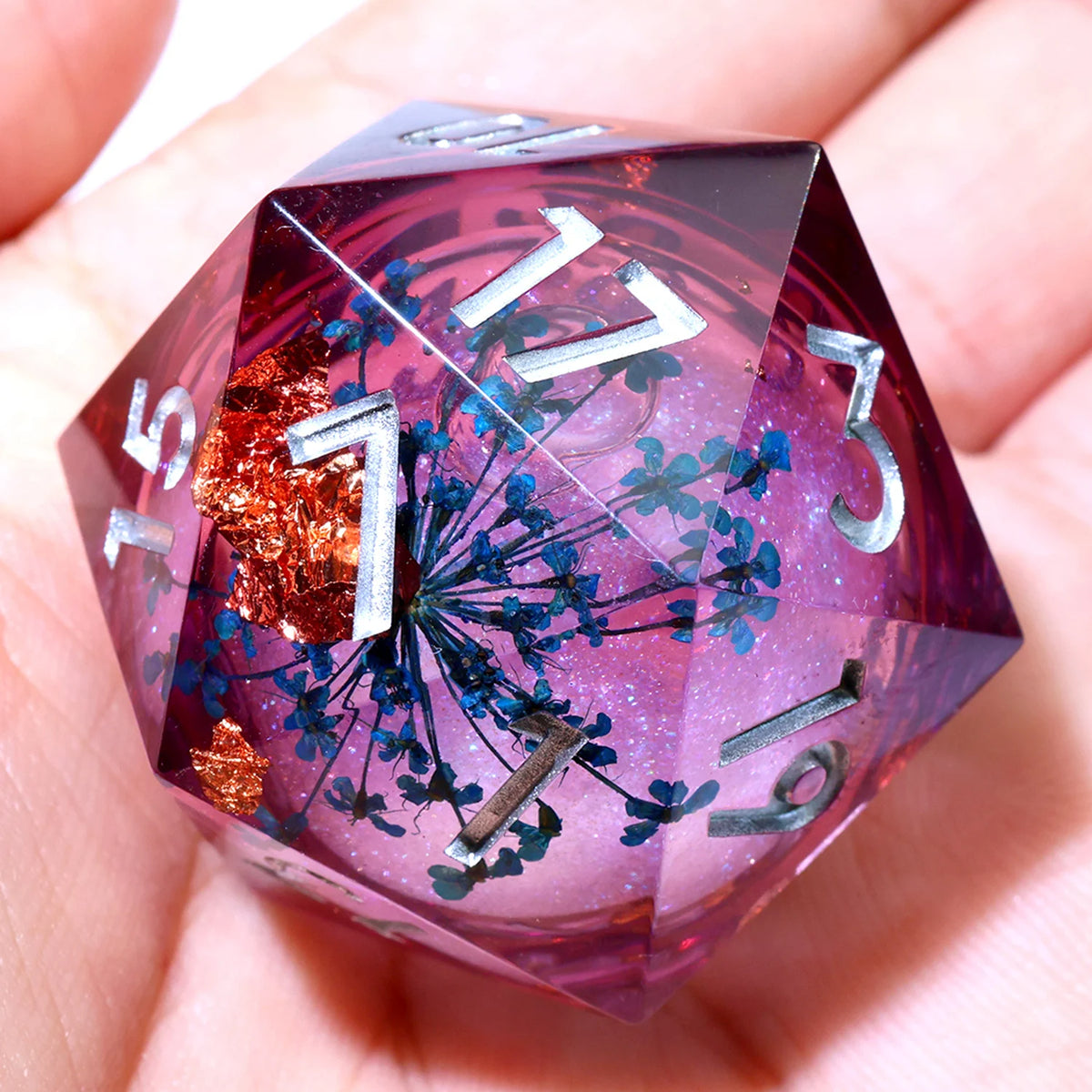 A handmade resin D20 die with a large blue and purple liquid swirl, held in a person's hand.