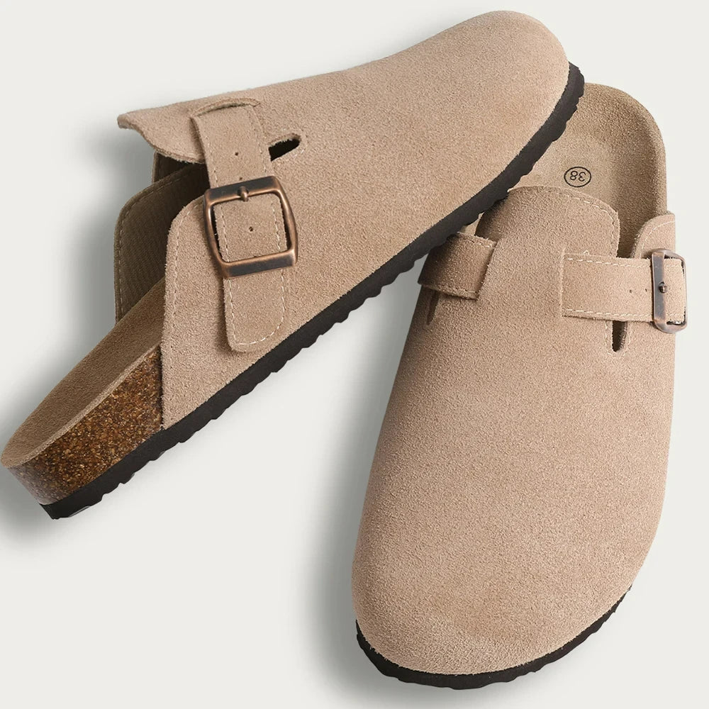 A pair of beige suede cork mules with leather straps and arch support shown from the side.