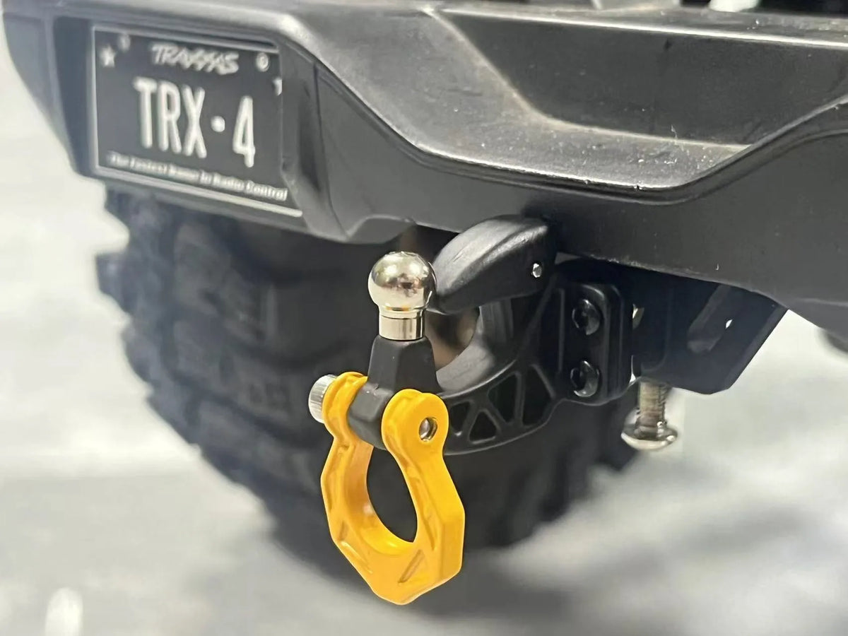 Close-up of a black metal trailer hitch receiver TRX-4 for an RC crawler car, showing the yellow mounting bracket.