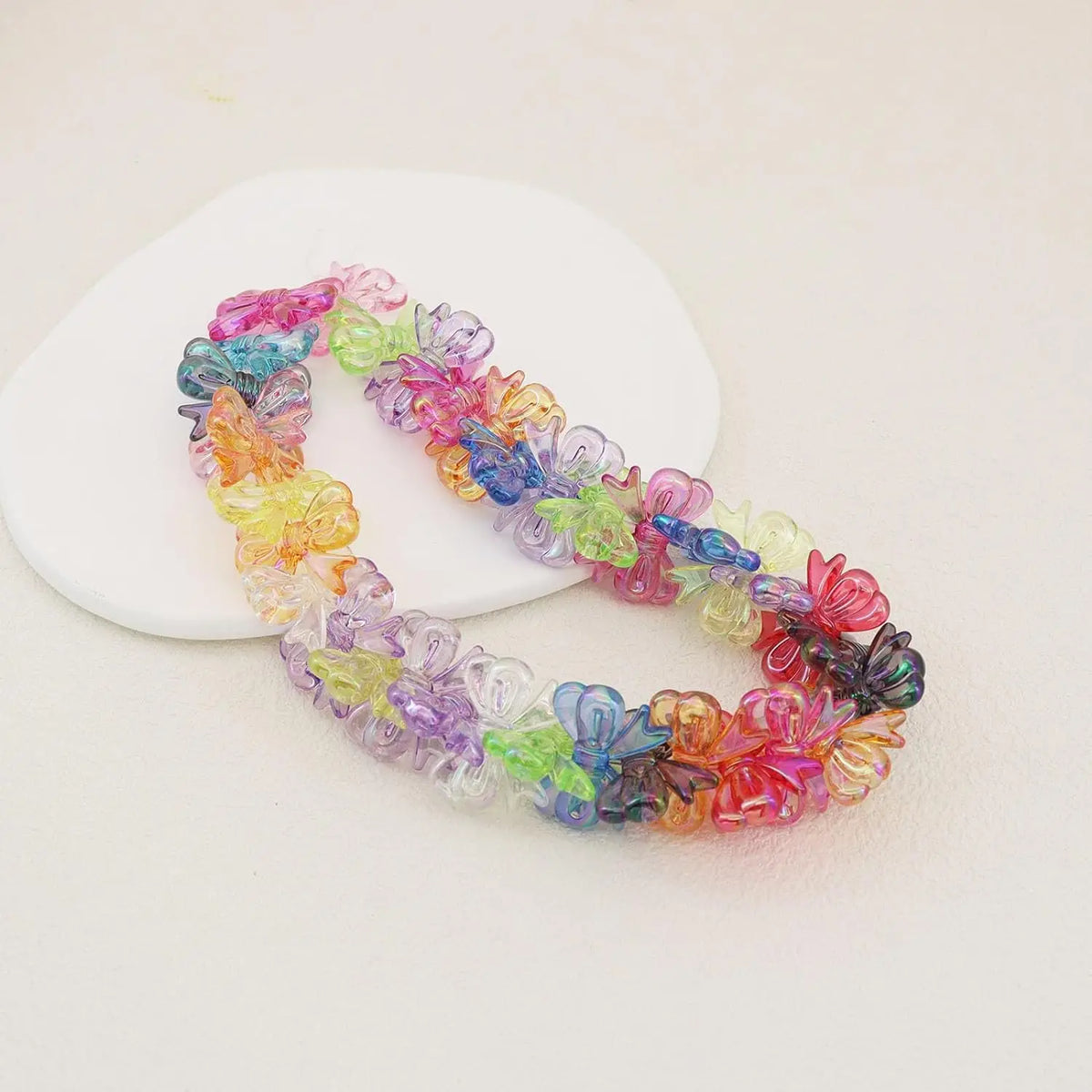 A string of colorful acrylic bow beads in shades of pink, purple, blue, and green laid on a white surface.