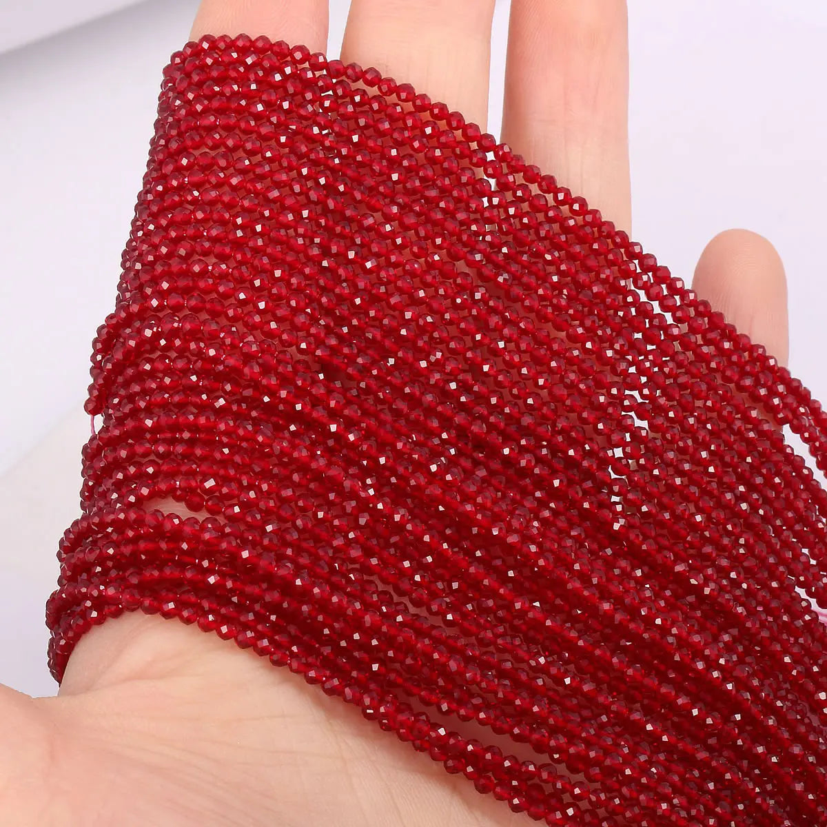 A close-up of a thick strand of faceted natural red beads being held in a hand.