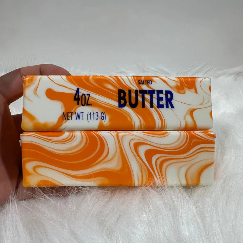 A rectangular butter stick fidget toy with orange and white marbled texture is held in a hand.