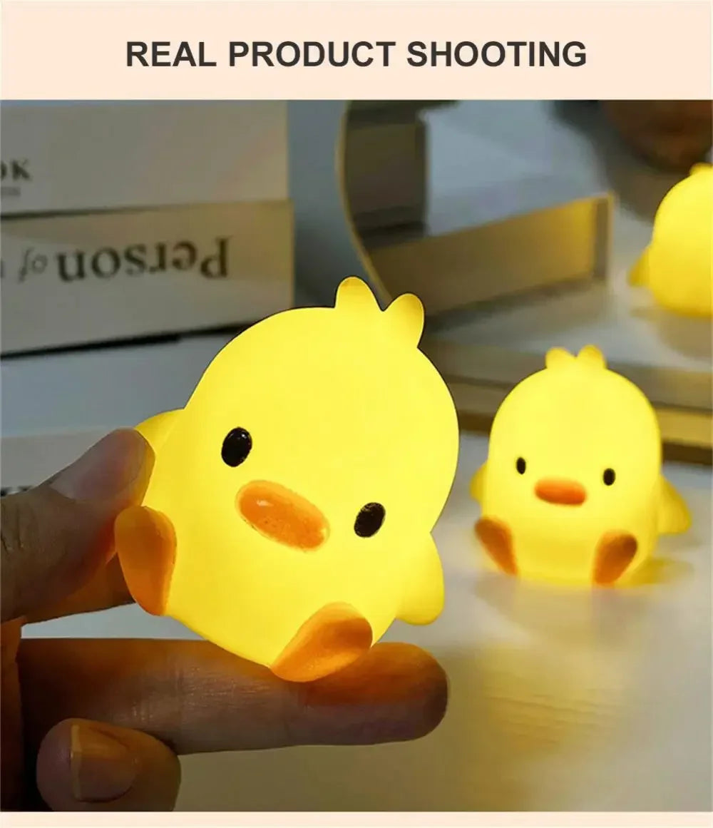 A hand holds a glowing yellow cartoon duck night light, illuminating a dark surface.