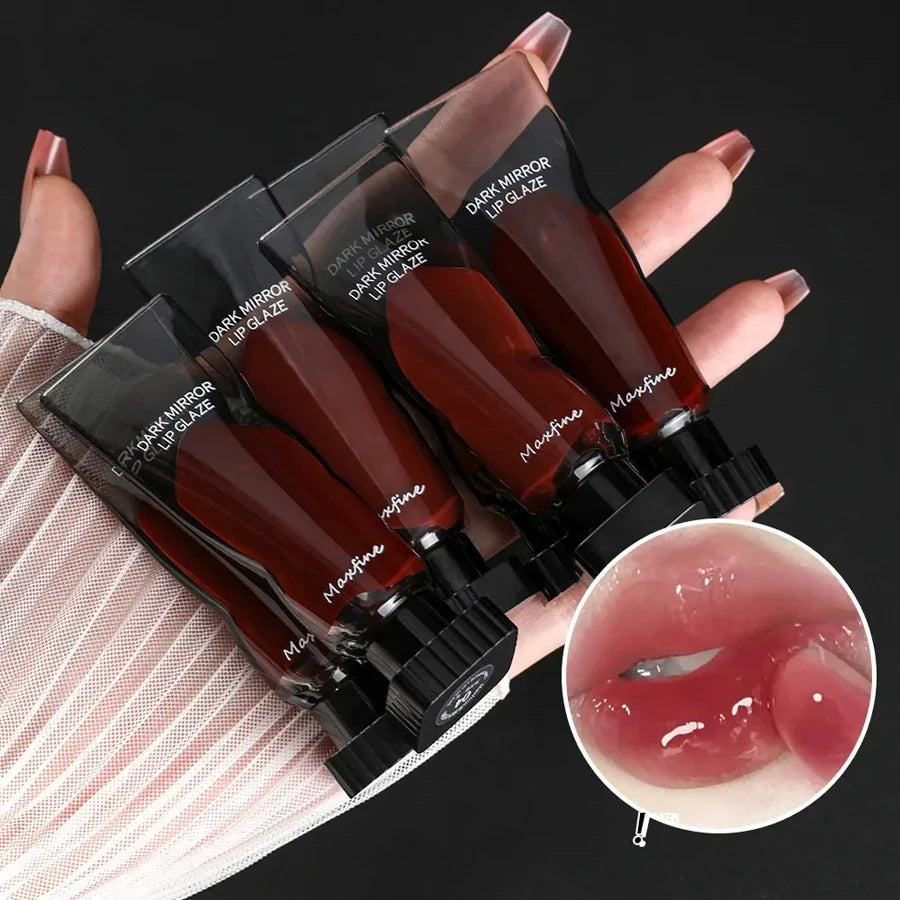 A hand holds several dark mirror lip glaze bottles with a maroon liquid and black caps against a light pink fabric.