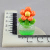 A miniature orange and yellow flower arrangement in a green glass pot resting on a ruler.