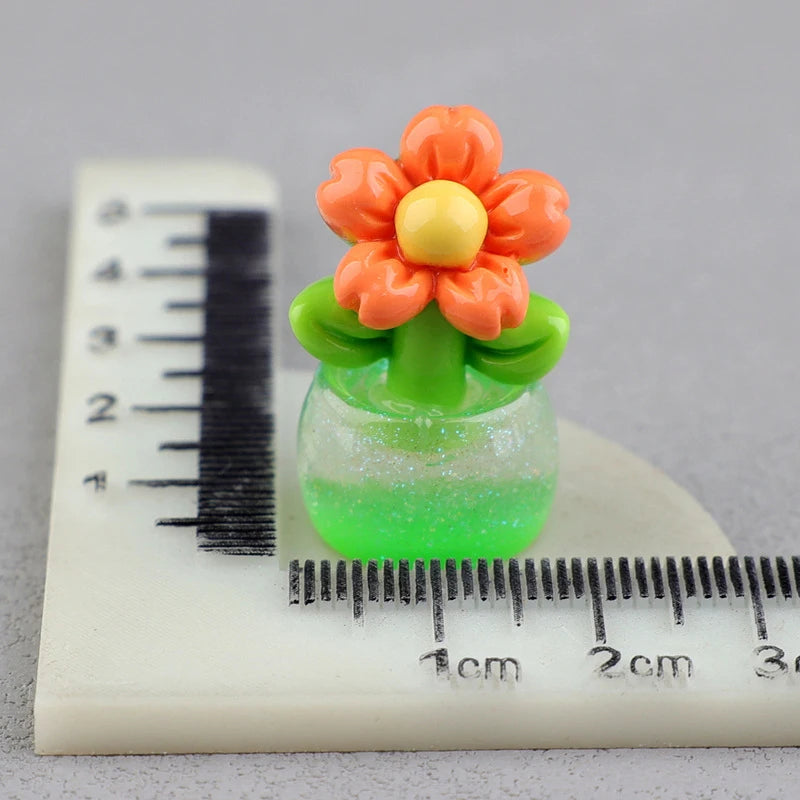 A miniature orange and yellow flower arrangement in a green glass pot resting on a ruler.