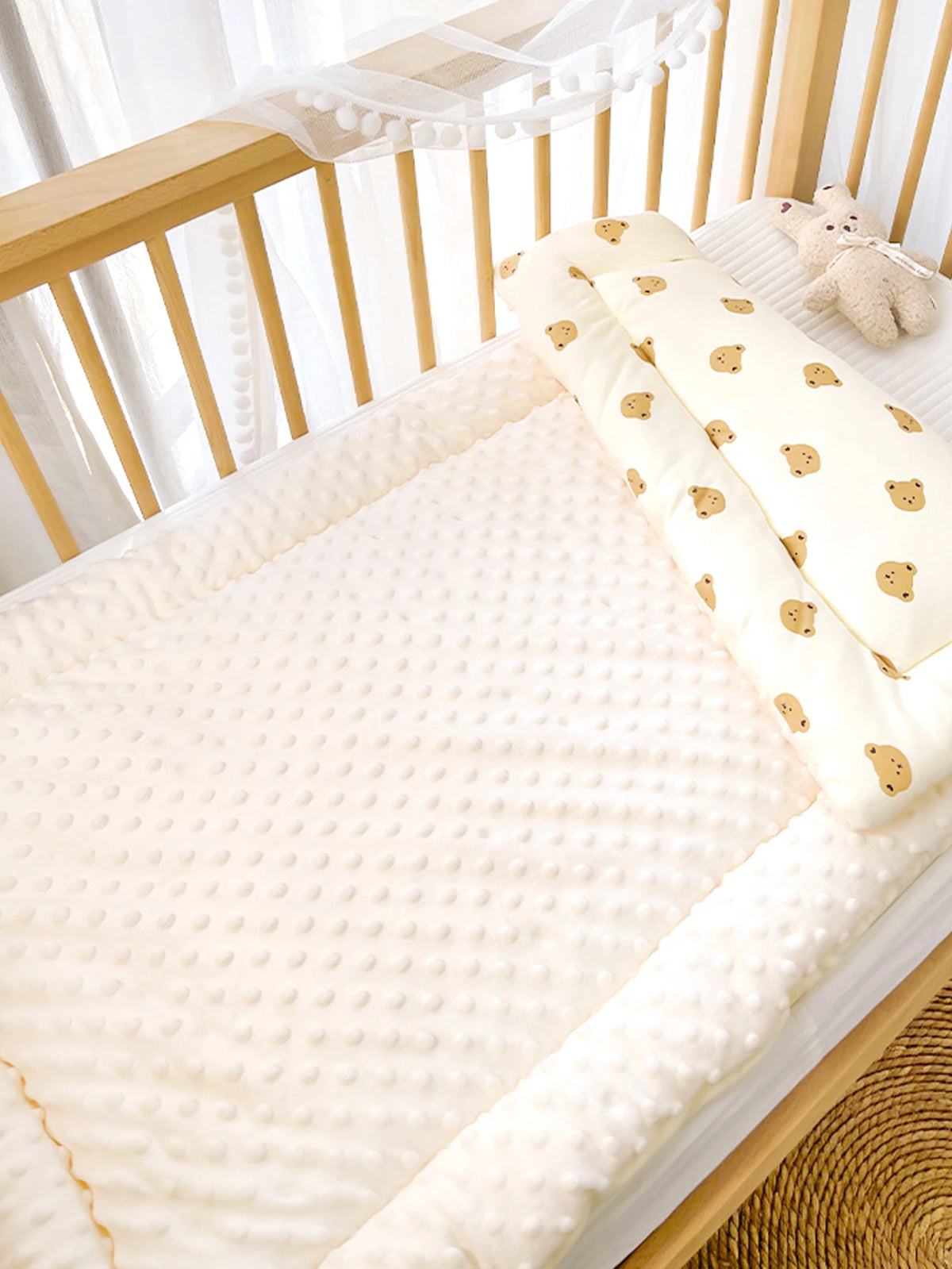 A soft fleece beanie blanket with yellow and brown bear patterns is displayed on a wooden crib railing.