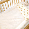 A soft fleece beanie blanket with yellow and brown bear patterns is displayed on a wooden crib railing.