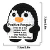 A handmade crochet penguin doll with black and white markings holding a card that reads Stay Positive & Waddle Your Own Way