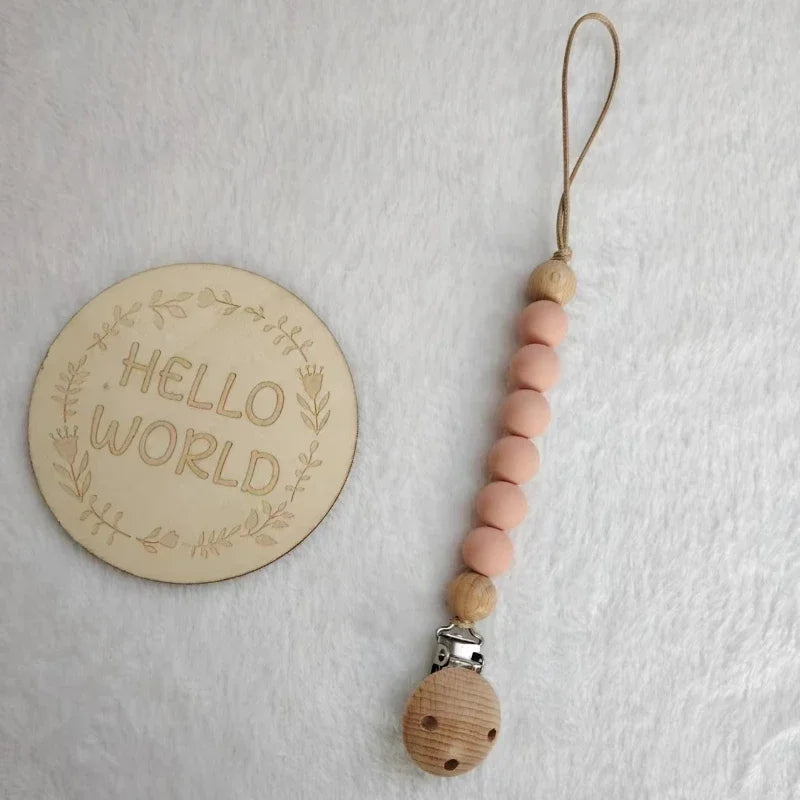 A string of light pink wooden beads attached to a clip for a pacifier or teether.