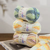 A stack of three balls of gradient acrylic yarn in various shades of green, yellow, and blue.