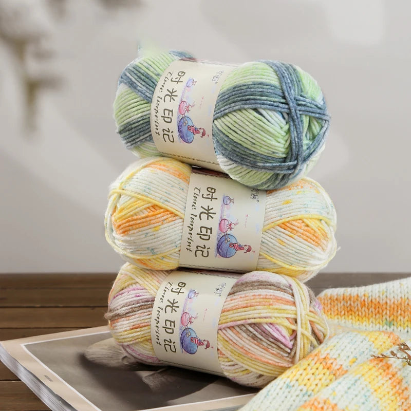 A stack of three balls of gradient acrylic yarn in various shades of green, yellow, and blue.