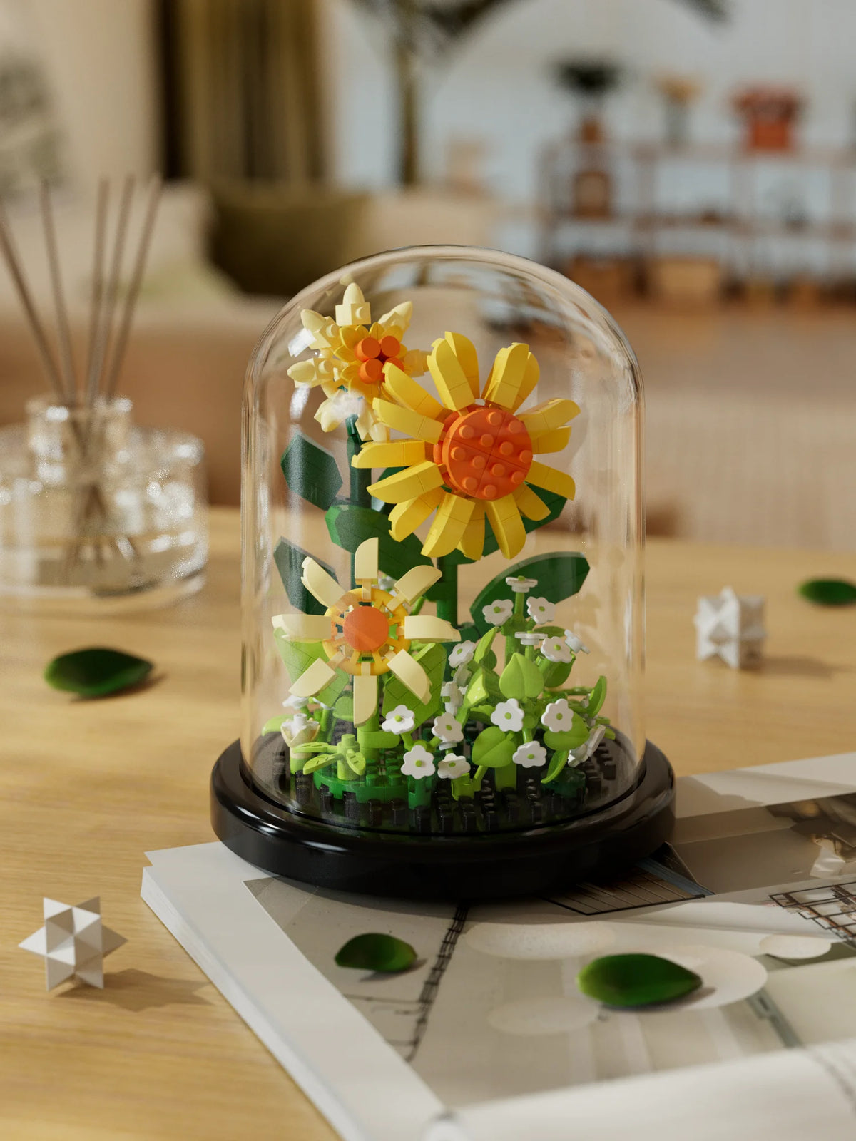 A glass dome display of a buildable eternal rose flower kit featuring yellow and orange flowers and green foliage.