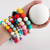 A hand holds a bracelet made of colorful silicone beads and a large white bead.