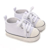 A pair of white canvas first walkers for infants, shown from the side.