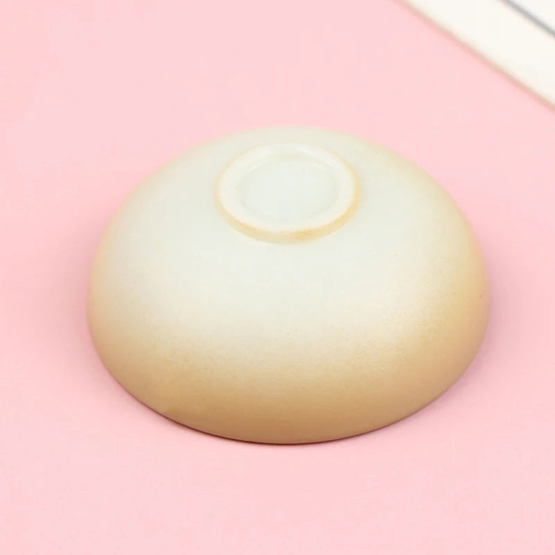 A smooth, beige miniature dollhouse rice bowl is shown against a light pink background.