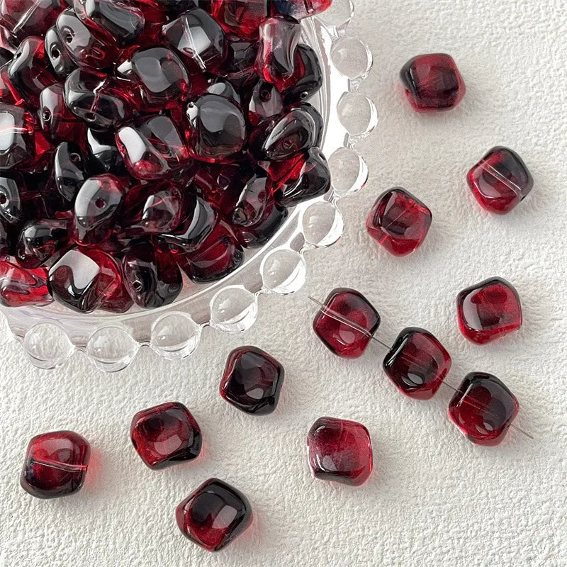 A pile of deep red geometric glass beads in irregular square shapes scattered on a white surface.