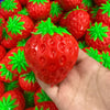 A hand holds a bright red strawberry stress ball surrounded by many similar squishy fidget toys.