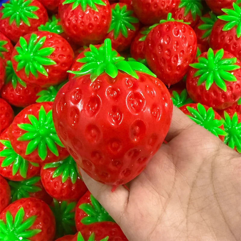 A hand holds a bright red strawberry stress ball surrounded by many similar squishy fidget toys.