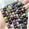 A hand holds a strand of natural stone beads including amethyst, garnet, and labradorite for jewelry making