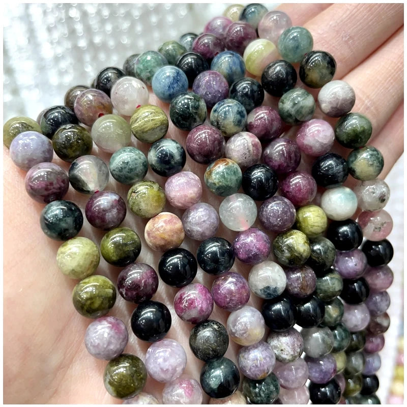 A hand holds a strand of natural stone beads including amethyst, garnet, and labradorite for jewelry making