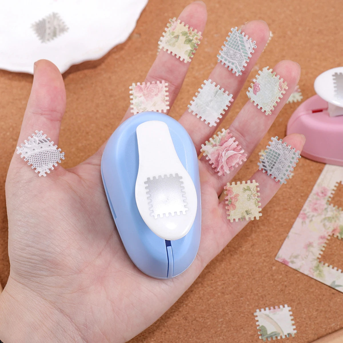 A hand holds a blue lever action embosser tool with various floral and patterned stamps on its surface.