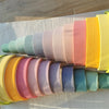 A collection of pastel wooden stacking blocks in a rainbow gradient, laid out on a light fabric.