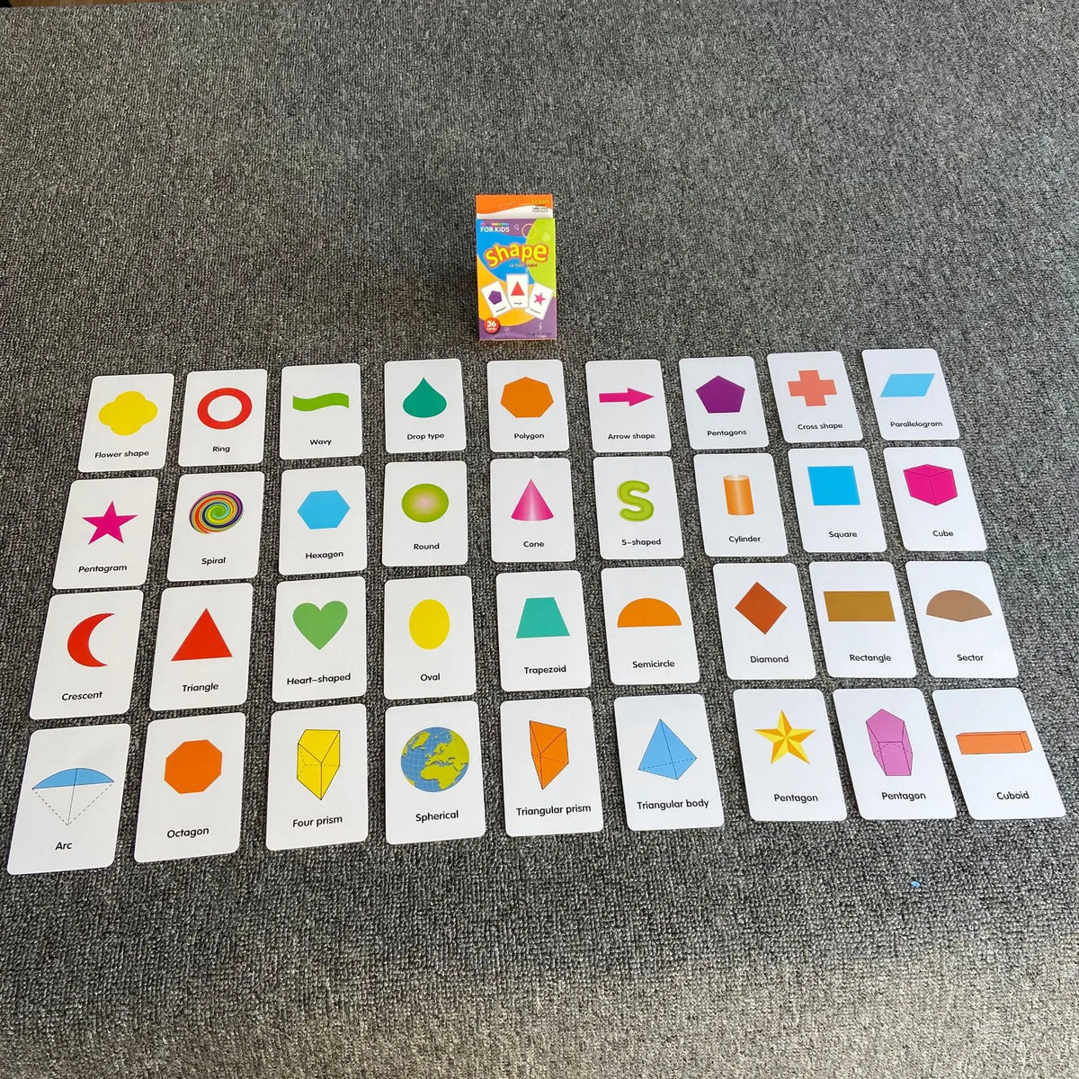 A collection of colorful learning flash cards featuring various shapes and geometric figures arranged on a gray surface.
