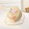 A round, handwoven straw crossbody bag with a lace pink and blue butterfly bow resting on a white surface.