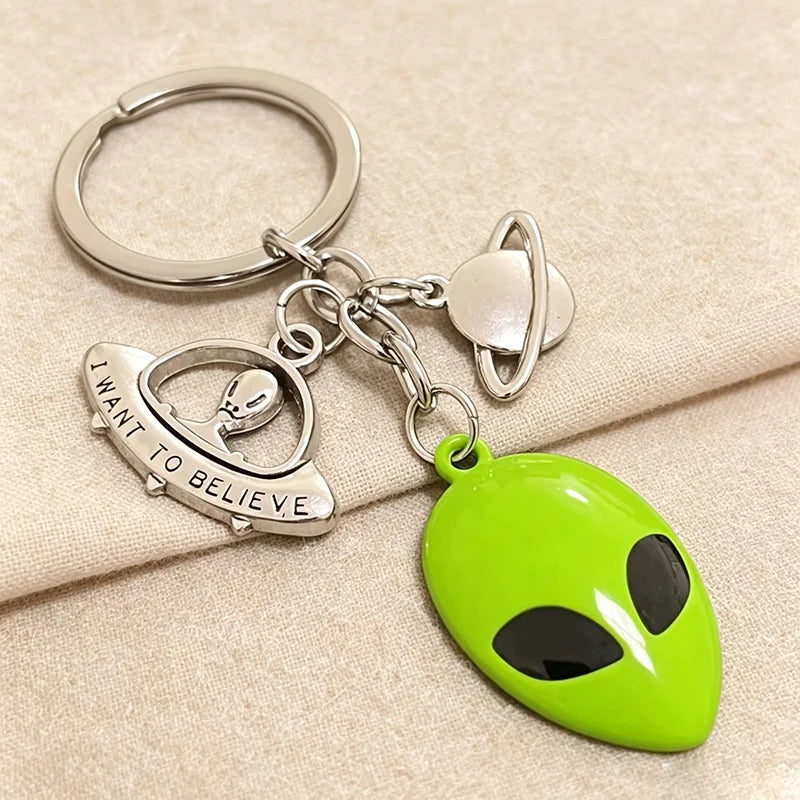 Silberner Schlüsselanhänger mit grünem Alien-Masken-Anhänger und silbernem Planeten-Anhänger.