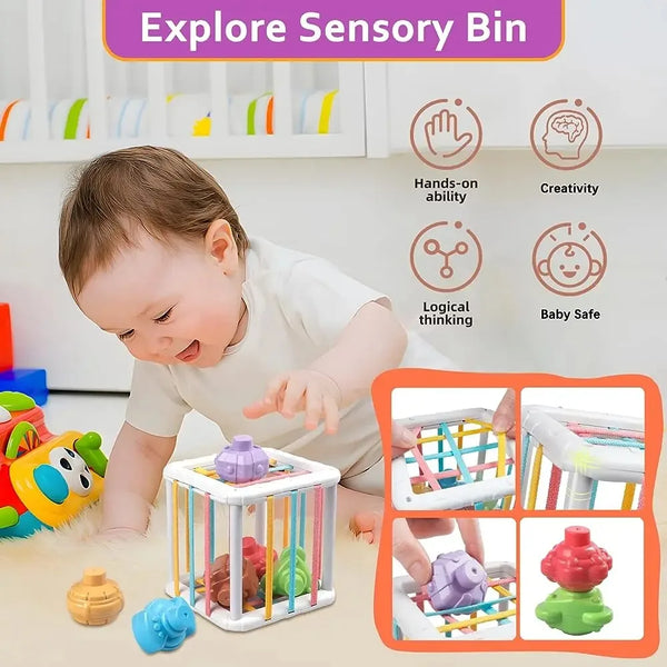 A toddler plays with a sensory bin containing colorful shapes and objects in a wooden cube sorter.