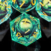 A close-up of a green liquid core resin die with the number 7 visible, surrounded by other polyhedral dice.
