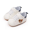 A pair of cream-colored baby sneakers with blue accents and a bear design for first walkers.