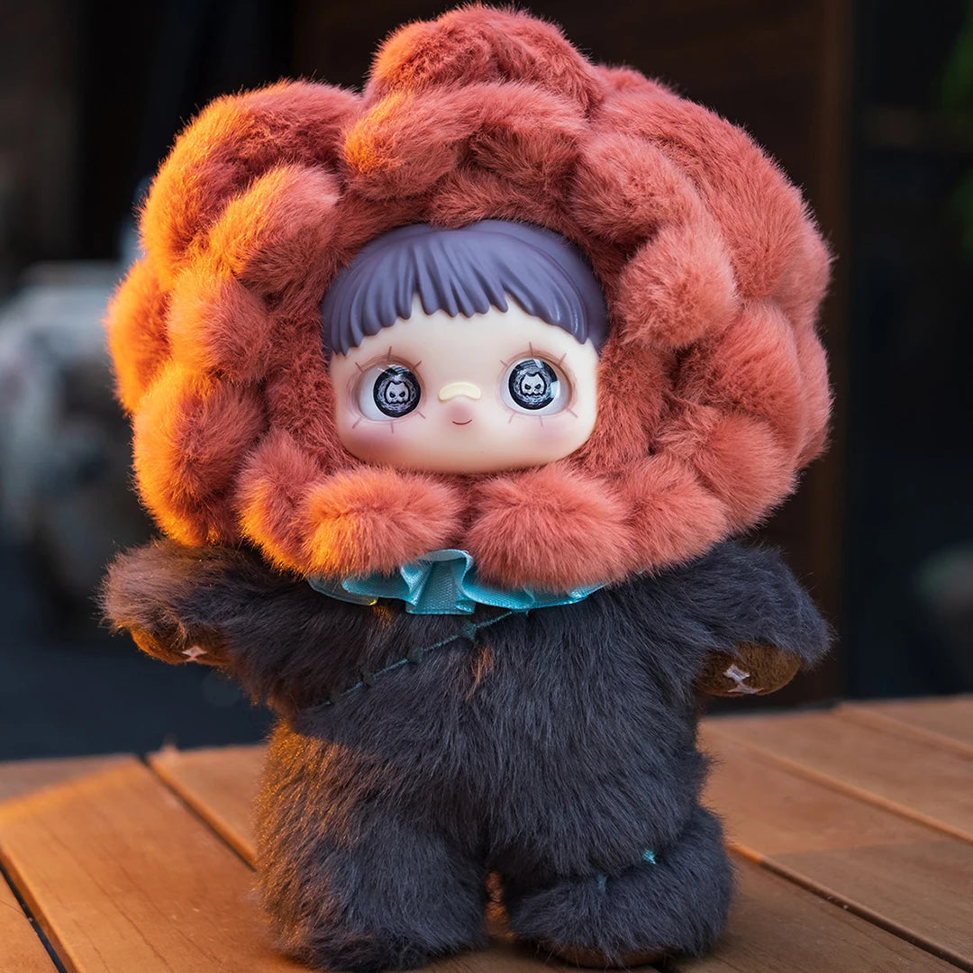A fluffy, reddish-brown plush doll with large blue eyes and a textured fur hood sits on a wooden surface.