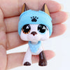 A small blue cat figure wearing a knitted hat and a blue collar is held in a person's hand.