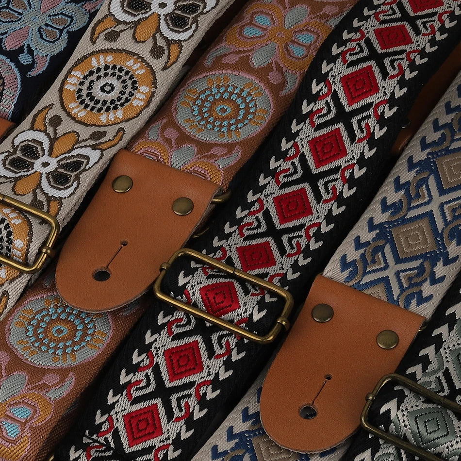 Close-up of an embroidered guitar strap featuring geometric patterns on fabric with brown leather ends.