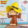 A collectible figure of Curious George in a yellow hat sitting on a wooden surface.
