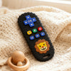 A black silicone teether shaped like a lion's face with various buttons and a remote control design resting on a cream-colore
