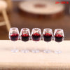 A set of five miniature clear resin wine bottles and cups with red liquid for a dollhouse display.