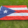 A large, folded Puerto Rico national flag featuring blue, white, and red stripes and a white star on a green lawn.