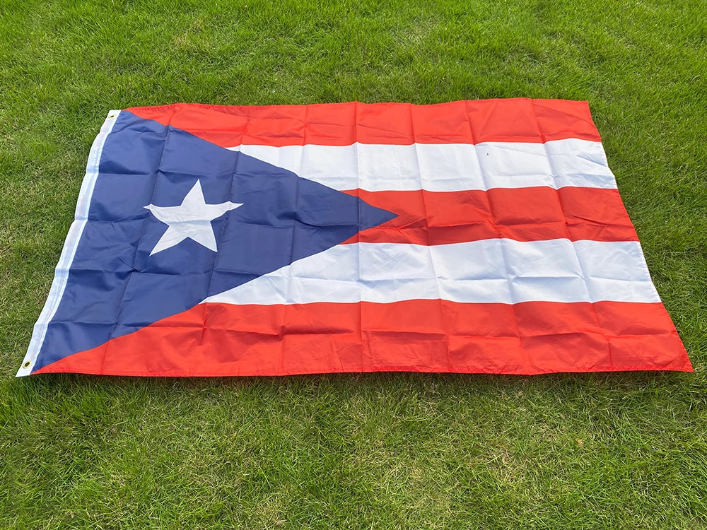 A large, folded Puerto Rico national flag featuring blue, white, and red stripes and a white star on a green lawn.